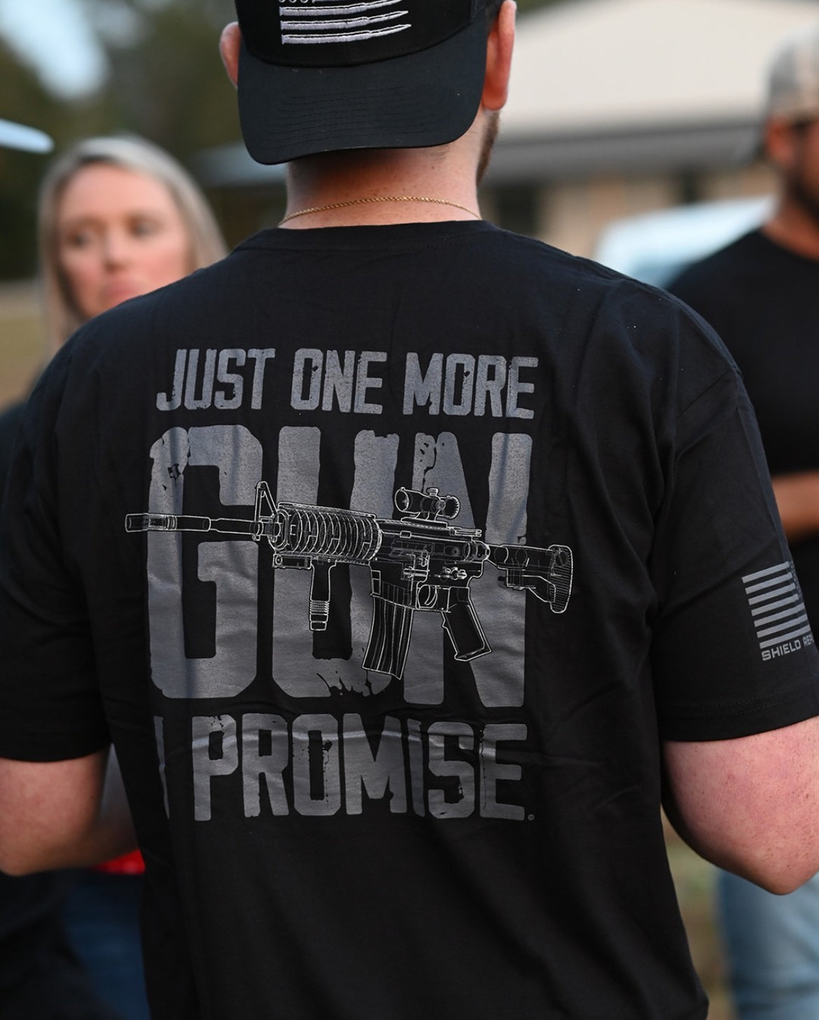 Person wearing a black t-shirt with a graphic and text on the back, standing outdoors.