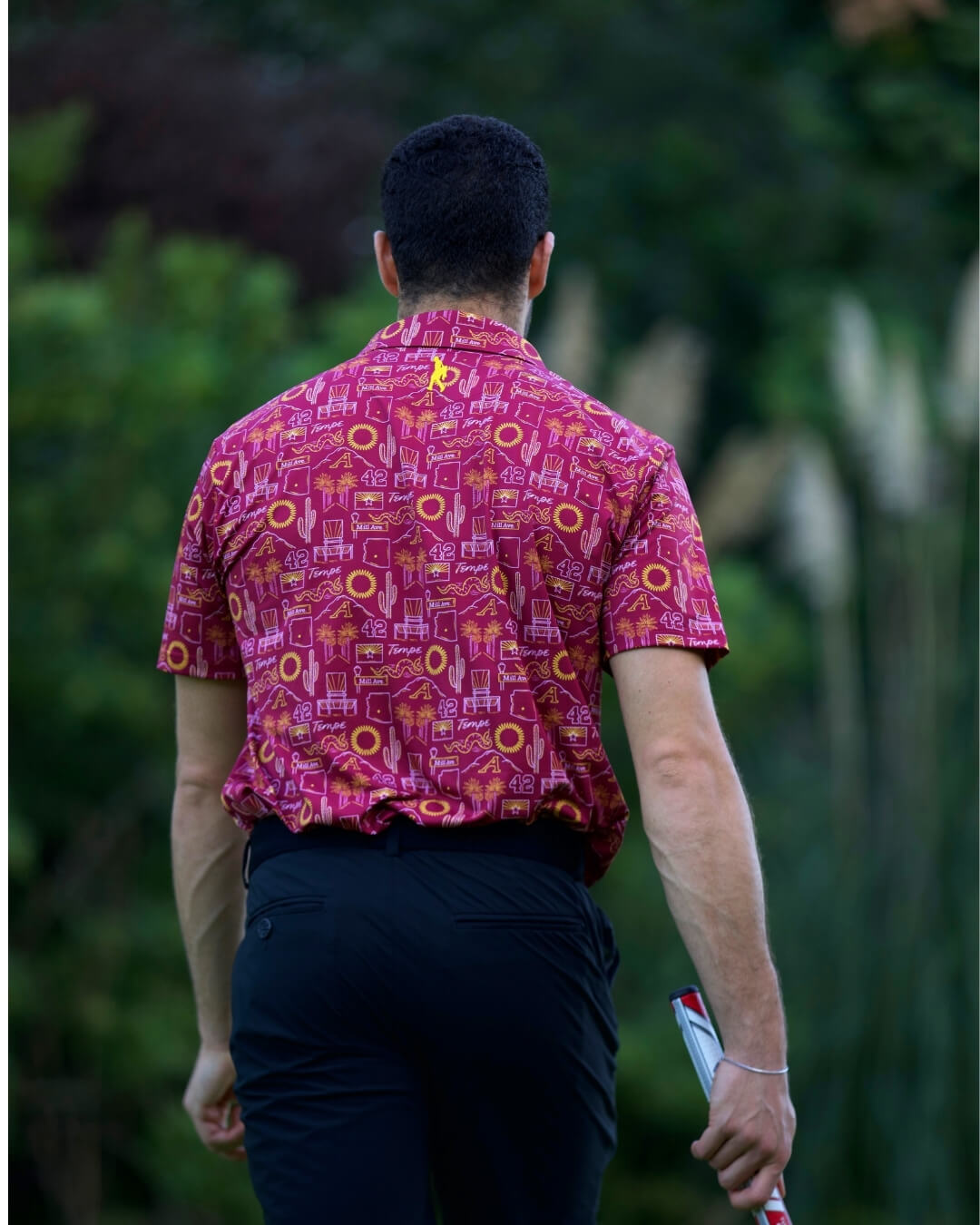 Back view of a man wearing a Tempe football polo shirt in a garden setting.
