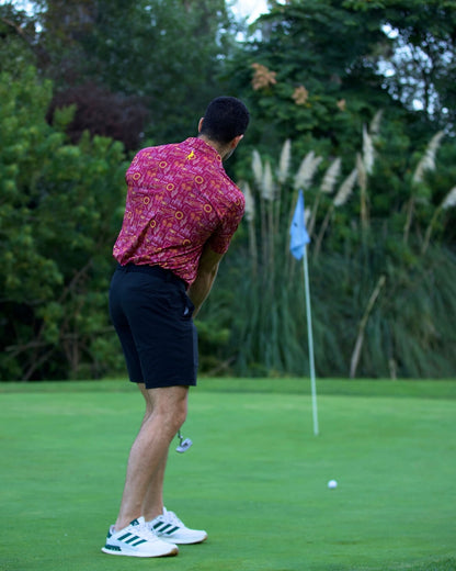 Man playing golf wearing Tempe football polo shirt, vibrant red design inspired by football culture, on a green course with a flag nearby.