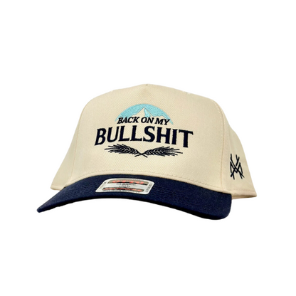 Front view of beige and navy trucker hat with 'back on my bullshit hat' embroidered, showing humorous and confident style.