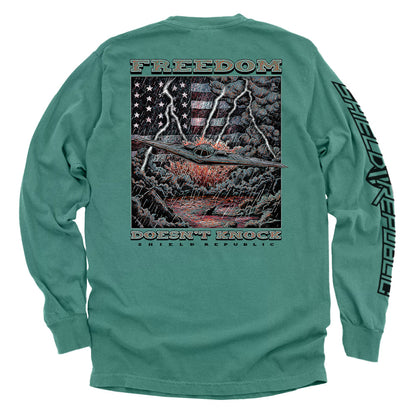 Freedom Doesn’t Knock Shirt with dramatic graphic and patriotic elements on a green tee, symbolizing strength and American resolve.
