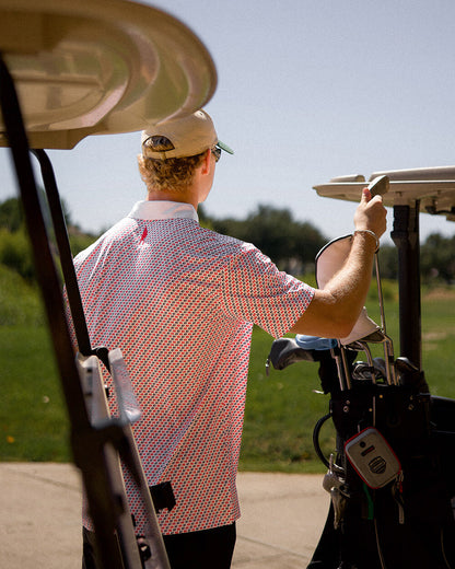 Man wearing a 45 47 polo shirt with a patriotic print, standing by a golf cart on a sunny day.