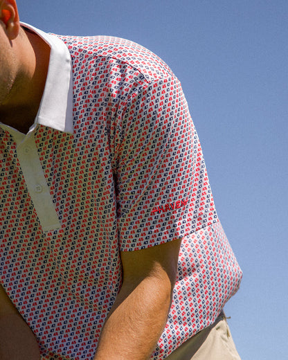 Close-up of a man wearing a 45 47 polo shirt with a red and navy pattern under a clear blue sky.